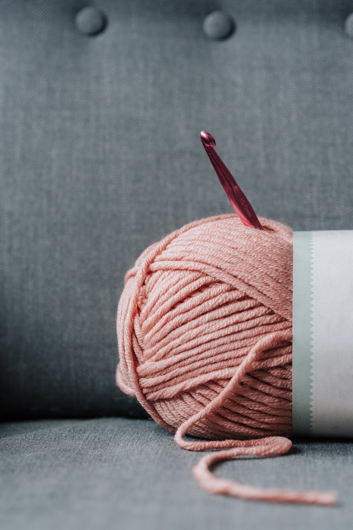 about-us Ball of soft yarn for knitting with pink crochet hook on gray comfortable couch at home